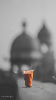 an orange drink sitting on top of a table next to a cup with steam coming out of it