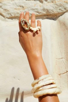 a woman's hand with rings and bracelets on her wrist, against a stone wall