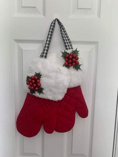 a pair of red mitts hanging on a white door with holly berries and mist