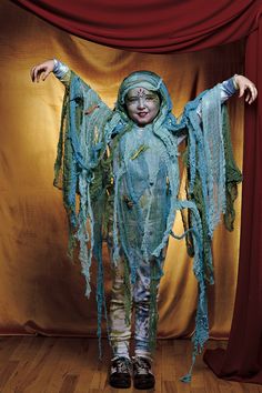 a child dressed as a scarecrow standing in front of a red curtain with her arms outstretched