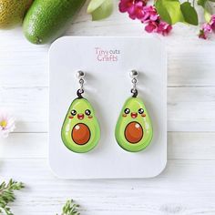 an avocado shaped earrings is sitting on top of a white table next to pink flowers