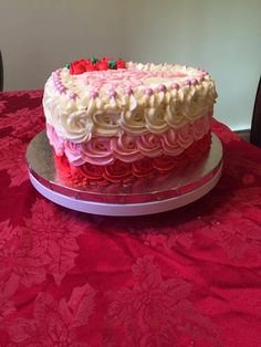 a cake with white and pink frosting sitting on a red tablecloth covered table