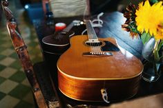 a guitar sitting on top of a wooden table next to a vase with sunflowers