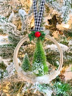 a christmas ornament hanging from a tree in front of snow covered evergreens