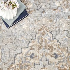 a blue and beige rug with white flowers on the floor next to a small book