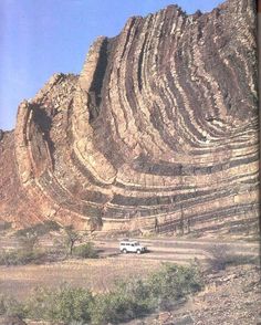 a truck is parked in front of a large rock formation on the side of a hill