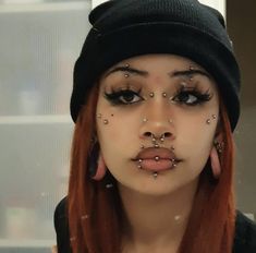 a woman with red hair and piercings on her nose wearing a black beanie