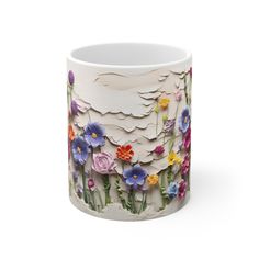 a white mug with colorful flowers painted on the outside and inside, sitting in front of a white background