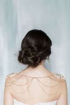 the back of a woman's dress with gold chains on her shoulders and shoulder