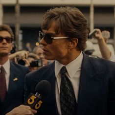 a man in a suit and tie holding a microphone while standing next to other people