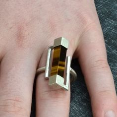 This is a very modern sterling silver ring with a square "tiger eye' with a strong chatoyancy, mounted between two square silver settings. The size of the top of the ring is app.1/2 inch (12mm) Tiger eye is classified as a semi-precious stone. It belongs to the chrysoberyl group. Since ancient times, chrysoberyl has been regarded as a gemstone which protects its wearer and keeps disaster at bay.  Material: Sterling Silver Finish: silky Size: 8 (different sizes on command) PLEASE SPECIFY YOUR EXACT RING SIZE. Because every ring is handmade by me, there will be slight variations on every ring I make, but the global design stays the same.  This ring will be shipped in a special made box, cushioned in coloured wool to protect and then re-boxed into a protective carton box.  I will ship every i Modern Silver Ring, Silver Jewelry Diy, Silver Jewelry Box, Jewelry Quotes, Silver Jewelry Design, Contemporary Ring, Modern Ring, Silver Rings Handmade, Ring Handmade