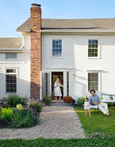 a man sitting on a bench in front of a house with a woman and child