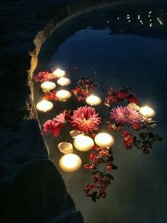 there are many lit candles in the water and flowers on the ground next to it