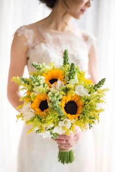 a bride holding a bouquet of sunflowers and greenery