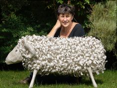 a woman sitting in the grass behind a sheep sculpture