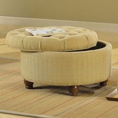 a round ottoman sitting on top of a wooden floor next to a table with a magazine