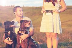 a man and woman holding two dogs in their hands while sitting on the ground with grass behind them