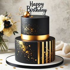 a black and gold birthday cake sitting on top of a white table next to a vase with flowers