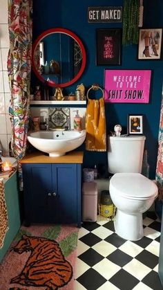 a bathroom with a checkered floor and blue walls is pictured in this image, there are pictures on the wall above the toilet