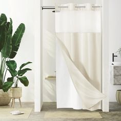 a white shower curtain in a bathroom next to a potted plant