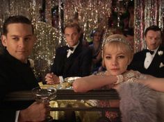 two men and a woman sitting at a table in front of a man wearing a tuxedo