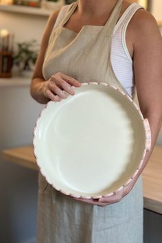 a woman in an apron holding a white plate with pink trimmings on it