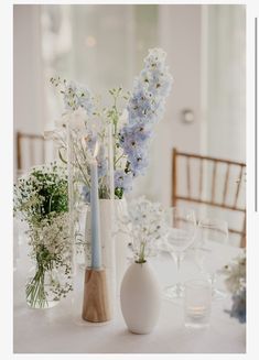 the table is set with white and blue flowers in vases, candles, and wine glasses