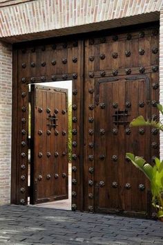 two large wooden doors are open in front of a brick wall and green plants on the sidewalk