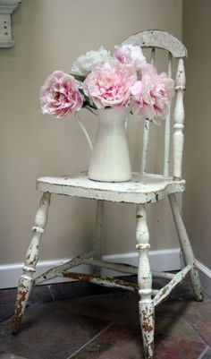 some pink flowers are in a white vase on an old chair