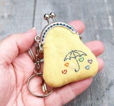 a hand holding a small purse keychain with an umbrella embroidered on the front