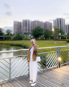 a woman standing on top of a bridge next to a body of water with tall buildings in the background