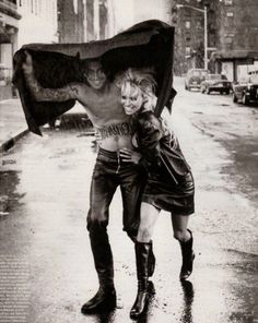 two people are walking in the rain with an umbrella over their heads and boots on