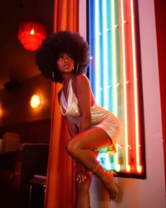 a woman posing in front of a window with neon lights on the wall behind her