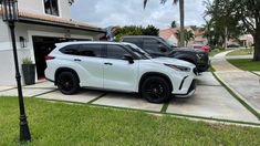 two white suvs parked in front of a house with palm trees and grass on the driveway