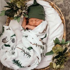 a newborn baby wrapped in a blanket next to flowers and greenery on a wicker basket