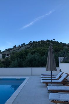 an empty swimming pool with lounge chairs and an umbrella in the foreground at dusk