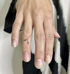 a woman's hand with a small black arrow tattoo on her left ring finger