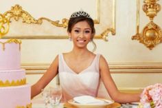 a woman sitting at a table in front of a pink and gold cake with flowers on it