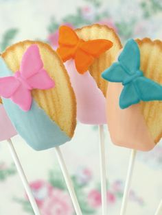 three cake pops with bows on them sitting in front of a floral wallpapered background