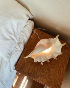 a wooden table with a light on top of it next to a white bed and pillows