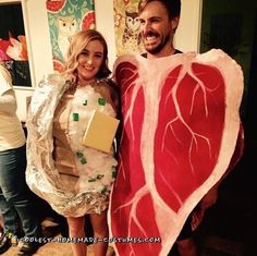 a man and woman dressed up in costumes standing next to each other holding large pieces of meat