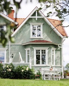 a house with green siding and white trim on the windows, grass in front of it