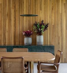 a dining room table with chairs and vases filled with flowers on the wall behind it