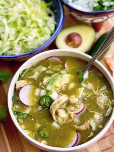 two bowls filled with soup and vegetables on top of a wooden cutting board next to an avocado