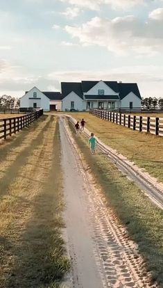 two people walking down a dirt road in front of houses