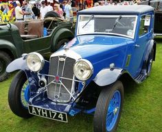 an old blue car parked on top of a lush green field next to other antique cars