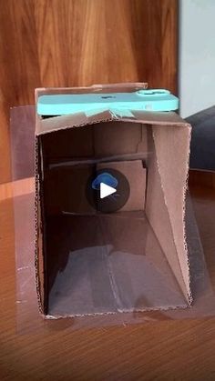 an open cardboard box on a table with a cell phone in the bottom corner and a video player inside