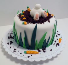 a cake decorated with grass, dirt and carrots on a white platter sitting on top of a table