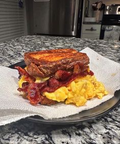 a breakfast sandwich with bacon, eggs and toast on a paper towel sitting on a plate