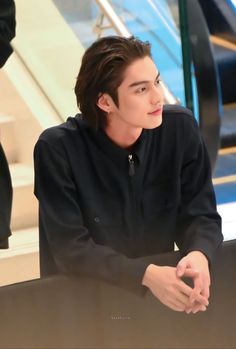 a young man sitting at a table with his hands on his knees and looking off to the side